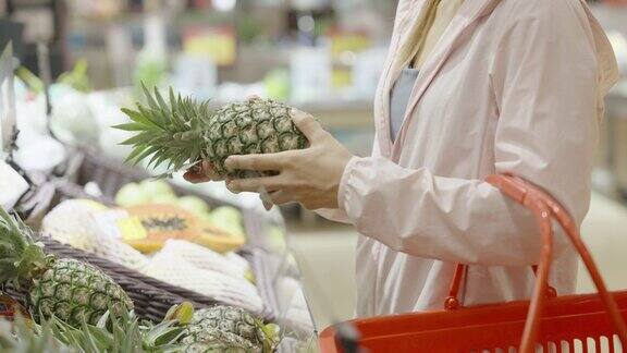 一名妇女在超市的水果摊上挑选菠萝特写