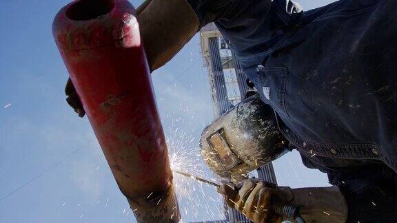 在一个阳光明媚的日子里一名油田工人在一个石油和天然气钻井平台上的井架旁焊接两根管道火花四溅