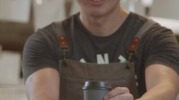 亚洲男咖啡师穿着拿着热咖啡杯在咖啡店为顾客服务