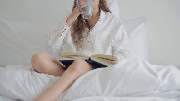 年轻女子早上坐在床上一边喝咖啡一边看书