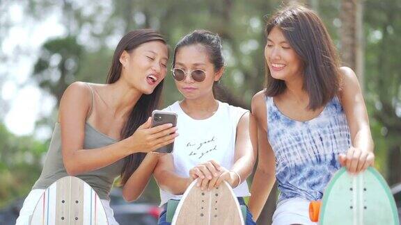 一群快乐的亚洲女性朋友在玩完滑板后坐在沙滩上聊天