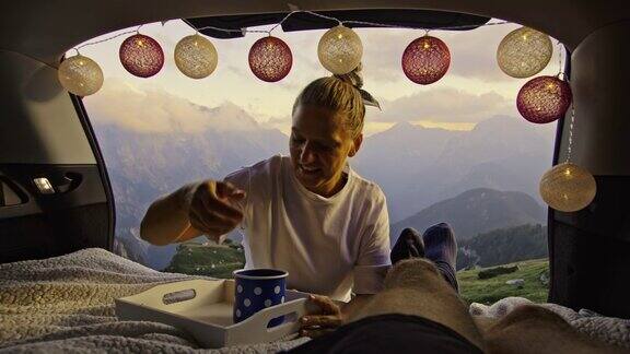 SLOMO女露营者在车里给她的伙伴带咖啡享受在山上的早晨