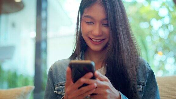 快乐年轻的亚洲美女使用智能手机和喝咖啡的咖啡馆