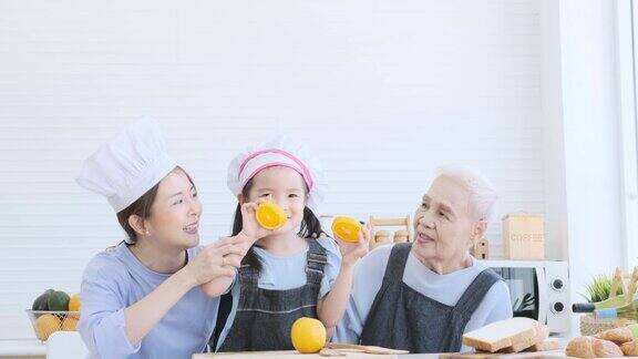 小女孩拿着橘子蒙着眼睛在厨房里和妈妈、奶奶玩