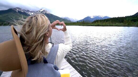 年轻女子站在湖边的木制码头上她做心型框架
