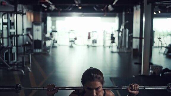 年轻女子在健身房里背扛杠铃做深蹲