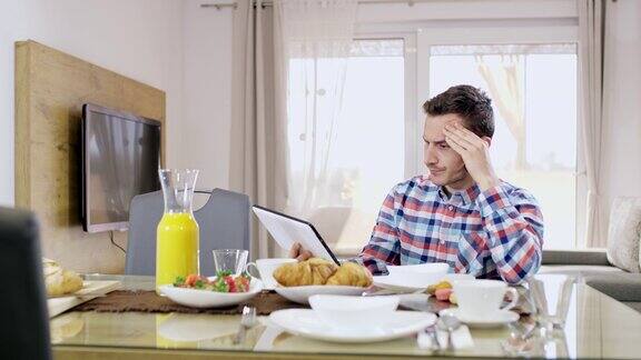 一名愤怒的年轻人一边吃早餐一边用平板电脑