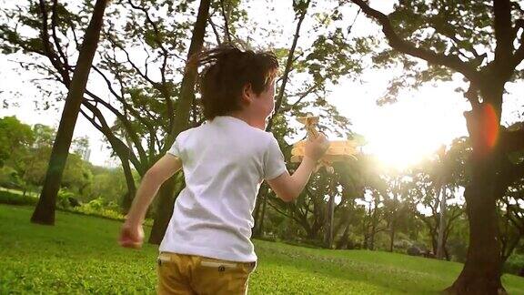 一个穿着白色衬衫的男孩在花园里奔跑手里拿着一架木制飞机一个儿童玩具在太阳即将升起的时候向前奔跑传递着孩子们的想象力谁都想追随梦想