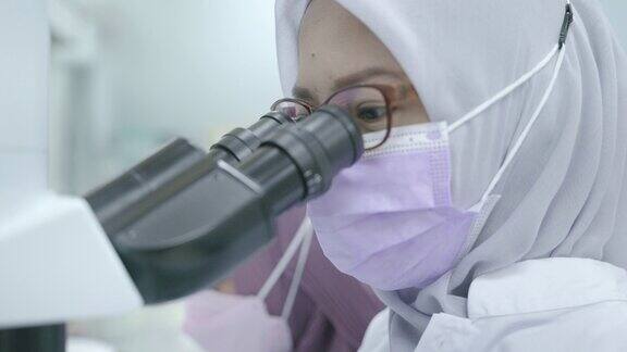 穆斯林女性研究员在实验室观察显微镜的场景