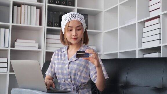 年轻的亚洲女子用信用卡和笔记本电脑在网上购物坐在酒店的床上