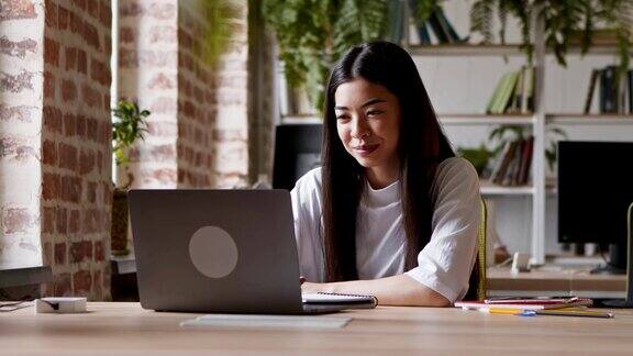 年轻的亚洲女孩通过电脑上的视频聊天与队友打招呼