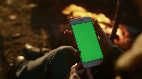 晚上女孩在篝火旁拿着一个绿色屏幕模型的肖像模式的智能手机