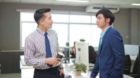 两个男同事在办公室里合作在办公室里交谈一起工作微笑着喝咖啡