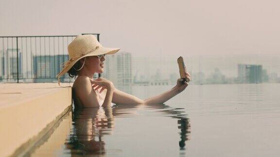 亚洲女性在屋顶酒店的游泳池里用智能手机自拍