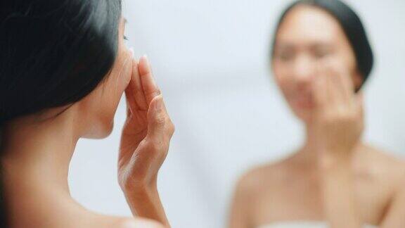 美丽的亚洲妇女肖像轻轻应用面霜面膜感性的触摸看在浴室的镜子年轻女性使皮肤柔软与天然化妆品护肤品的焦点