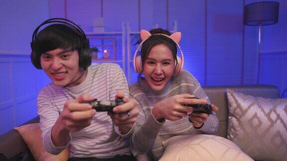 年轻的亚洲夫妇一家人在家里的客厅里用霓虹灯玩在线视频游戏