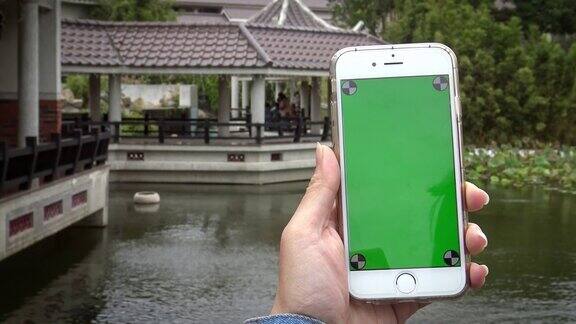 4K亚洲女人显示绿色屏幕手机在中国花园与小湖