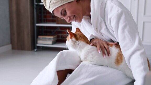 一个穿着浴袍的女孩喜欢和她的猫在一起她抚摸和亲吻她
