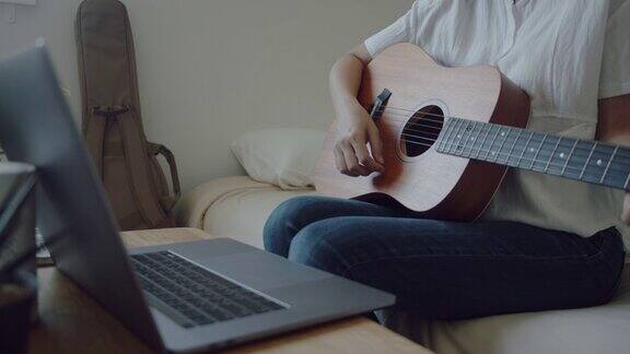 年轻女子一边玩原声吉他一边用笔记本电脑视频聊天