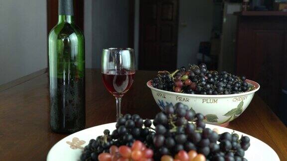 一堆新收获的葡萄放在陶瓷盘子和陶瓷碗里红酒装在玻璃杯里放在木桌上
