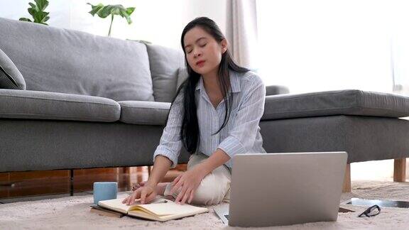 年轻的亚洲女商人正在笔记本上写一个新的项目她累了伸懒腰躺在客厅的沙发上在家工作商业女性和工作理念