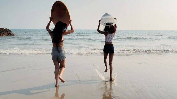 亚洲两个美丽的年轻女子冲浪女孩在沙滩上穿着比基尼和白色冲浪板体育cinemagraph
