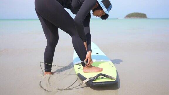 在沙滩上冲浪前一名亚洲女子将冲浪板安全腿绳戴在脚踝上