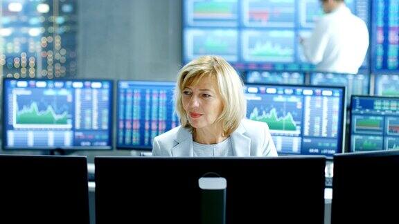 在市场交易室高级销售代表在她的工作站工作在后台监视器与股票号码数据和图表