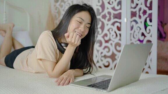 快乐的年轻女子躺在床上早上用笔记本电脑生活方式和在家放松与科技在家工作的自由职业者