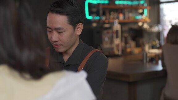 4K亚洲男子服务员服务咖啡拿铁和面包房在桌子上的女性顾客在咖啡店