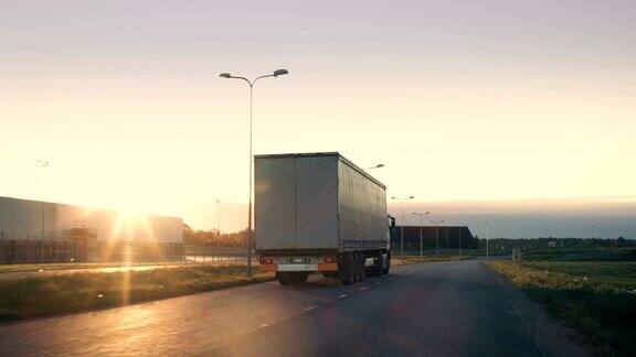 一辆带拖车的半卡车在高速公路上行驶的后续镜头一辆白色卡车在阳光照耀下的空旷道路上穿过工业仓库