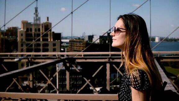 镜头跟随美丽快乐的欧洲黑发女商人戴着时尚的太阳镜走在布鲁克林大桥4K