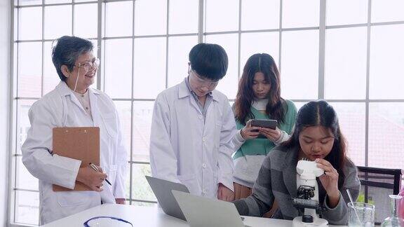 女学生用显微镜做实验在笔记本电脑和平板电脑上记录下她们看到的东西科学老师在旁边指导她们小学科学教室里的气氛