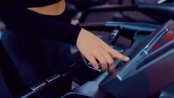 女孩跑到跑步机上按下模拟器上的按钮打开它健身器材特写