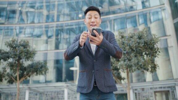 一个快乐而兴奋的商人站在城市里用着智能手机一个自信的年轻商人在城市背景下的网络工作中获胜并庆祝