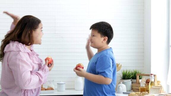 胖妈妈和胖男孩在厨房吃一个苹果有机营养维生素C饮食观念