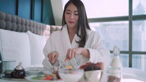 亚洲女人穿着睡衣在床上吃早餐在一个豪华酒店在市中心的度假旅行期间