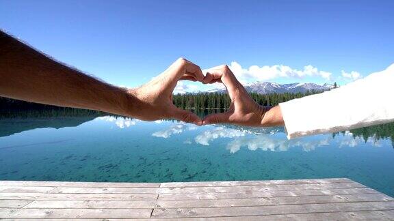 一对夫妇的手在湖边做了一个心形的框架