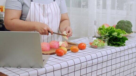 亚洲孕妇在厨房从网上学习如何做健康的食物肥胖的妇女准备蔬菜沙拉作为减肥食品和减肥健康饮食