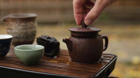 特写镜头一只手合上了泡普洱茶的陶制茶壶的盖子户外中国茶道