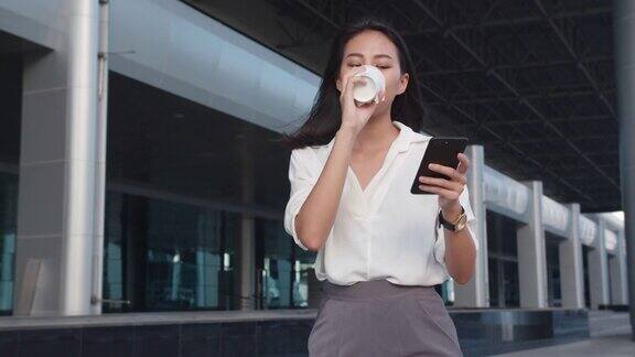 亚洲女商人穿着时尚的办公室服装拿着一次性纸杯热饮在城市现代城市的户外散步时使用智能手机