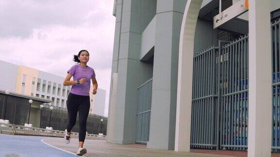年轻的女运动员在体育场的蓝色跑道上慢跑