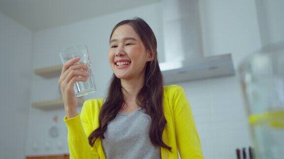 年轻的亚洲女子微笑着在厨房喝维他命水