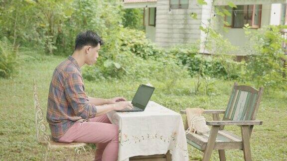 一名亚洲男子在户外咖啡馆使用笔记本电脑工作
