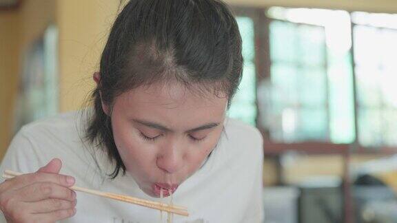 在室内亚洲妇女用筷子在碗里吃面条