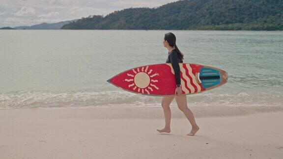 亚洲运动女子手持冲浪板在沙滩上行走