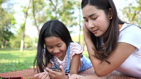 亚洲小女孩和年轻的母亲在花园里使用手机进行电子学习