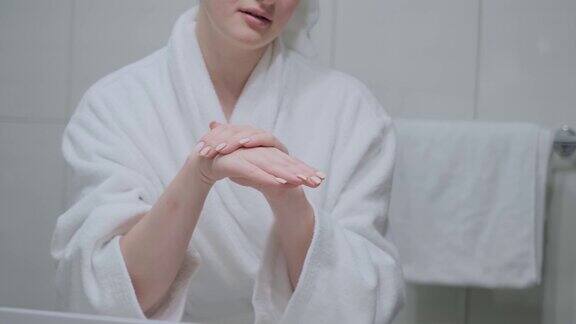 女孩在手上涂上乳霜按摩穿着白色浴袍浴室手部护肤保湿护肤霜特写
