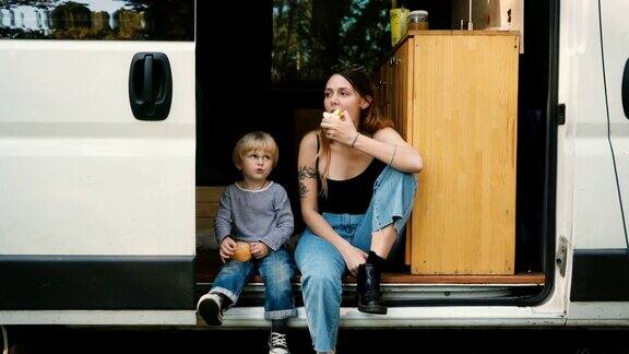 带着儿子坐在露营车里吃苹果的女人