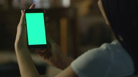 少女拿着智能手机与绿色屏幕在肖像模式在晚上休闲的生活方式
